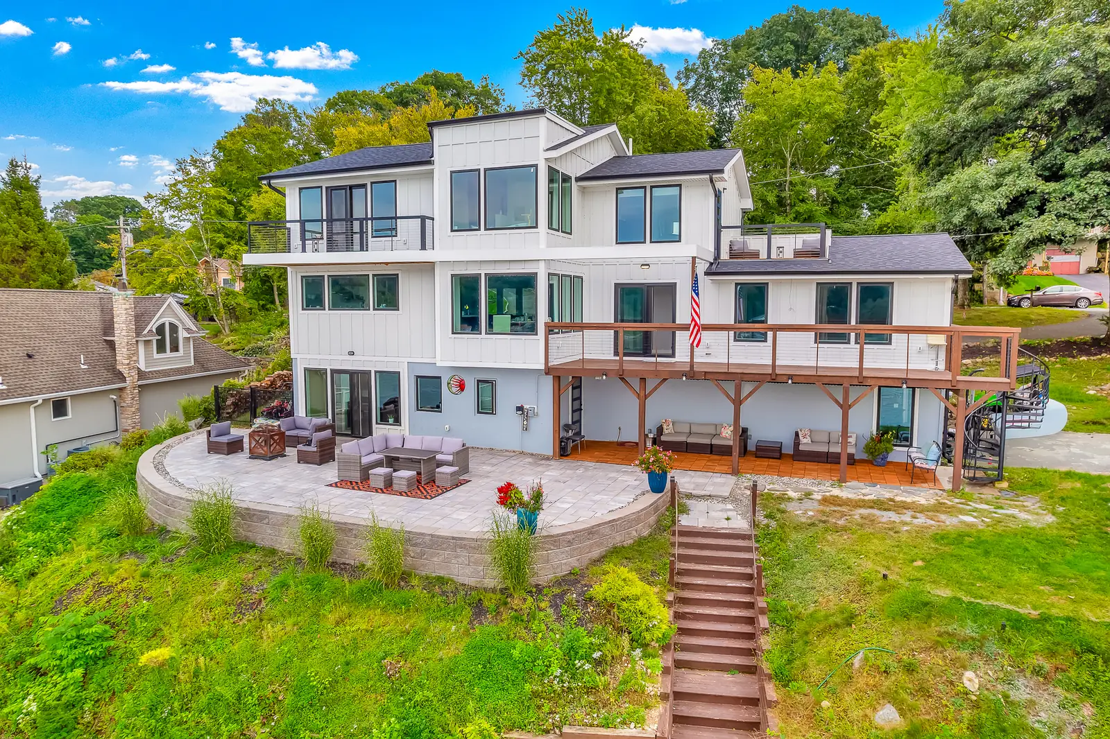 The house from the air above the lake, three storeys of white board and glass above a curved stone patio
