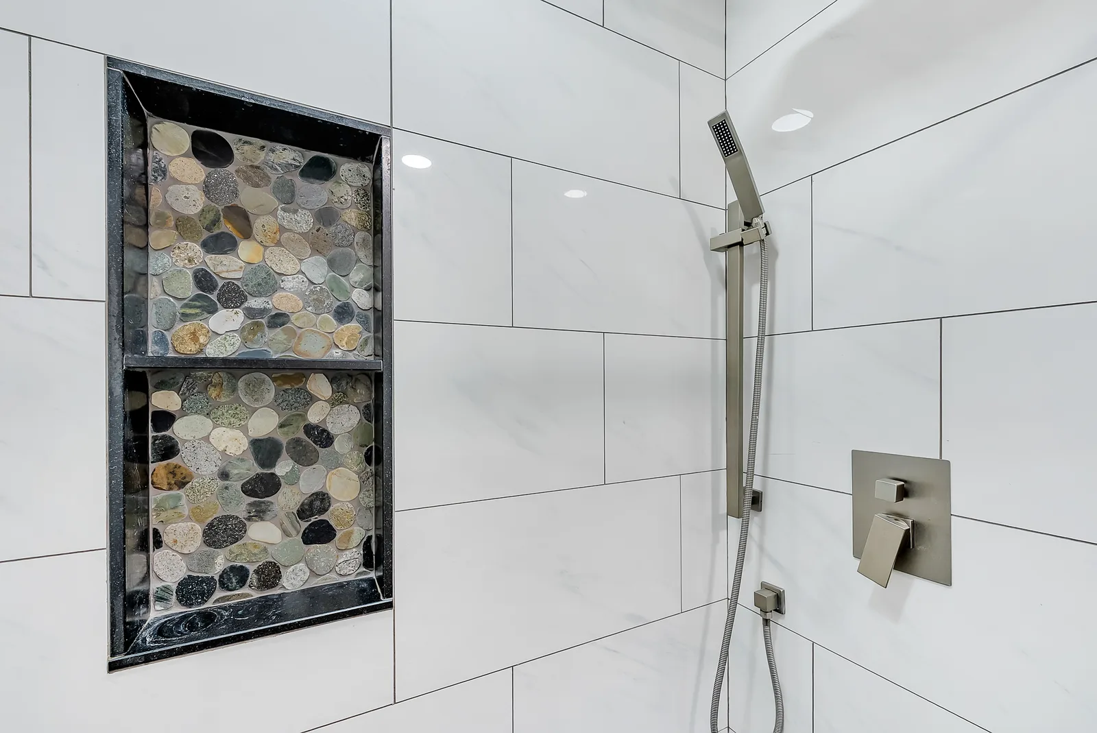 A walk-in shower, a panel of dark river-stone mosaic set into white tile with matte black fittings