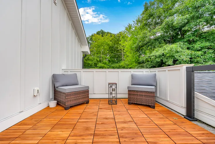 A teak deck with two chairs and a small table beside a covered hot tub, trees close on every side