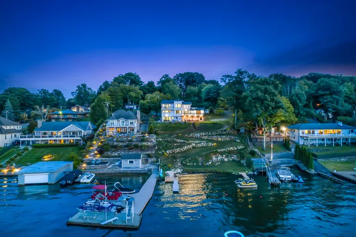 The shoreline from the air at dusk, lit windows along the bank and boats at their moorings