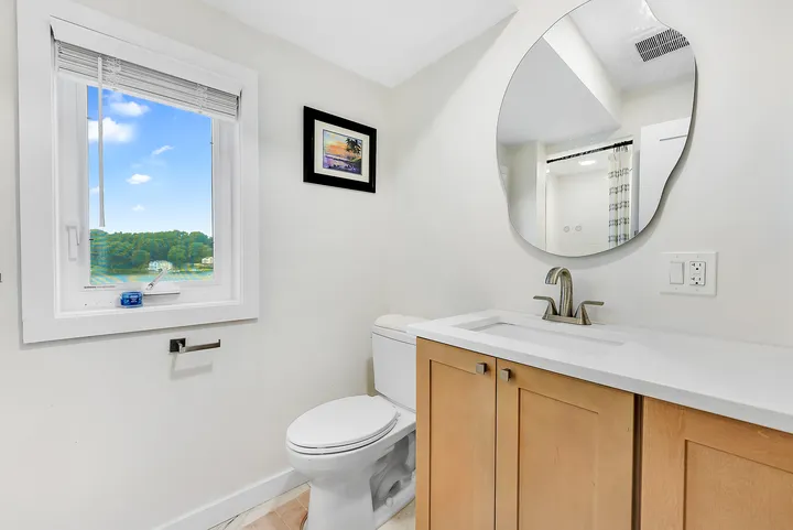 The retreat space's bathroom: a pale timber vanity with a stone top, a round mirror, and a window onto the trees